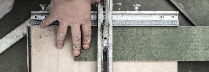 Eine Person schneidet eine grüne Fliese mit einem Fliesenschneider.